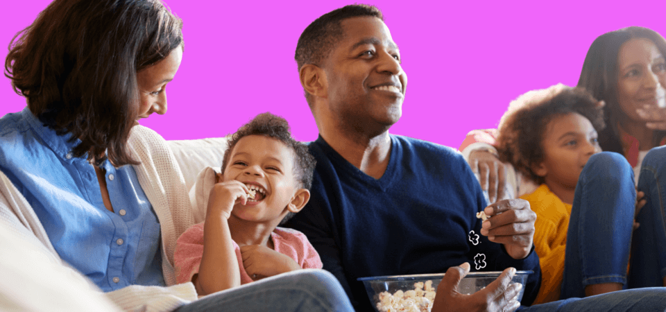 A family sitting on a couch, eating popcorn, and watching TV